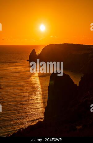 Un coucher de soleil rouge avec la silhouette d'une falaise au-dessus de la mer Banque D'Images