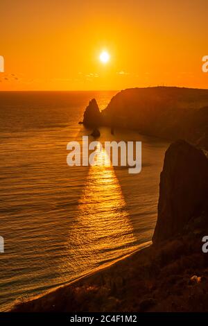 Un coucher de soleil rouge avec la silhouette d'une falaise au-dessus de la mer Banque D'Images