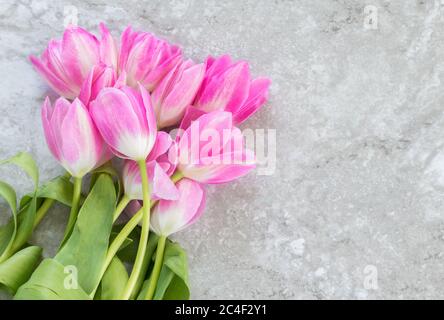 un bouquet de tulipes roses délicates avec des tiges et des feuilles vertes sur fond de marbre gris avec espace de copie Banque D'Images