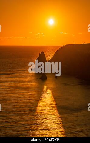 Un coucher de soleil rouge avec la silhouette d'une falaise au-dessus de la mer Banque D'Images