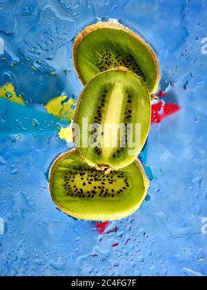 Les kiwis se tranches sur fond coloré et les gouttelettes d'eau, la couleur et la nourriture encore vie Banque D'Images