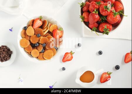 Bol maison sucré avec de minuscules crêpes au chocolat, au miel, aux fraises et aux myrtilles sur une table blanche. Pose à plat. Mise au point horizontale sélective. Banque D'Images