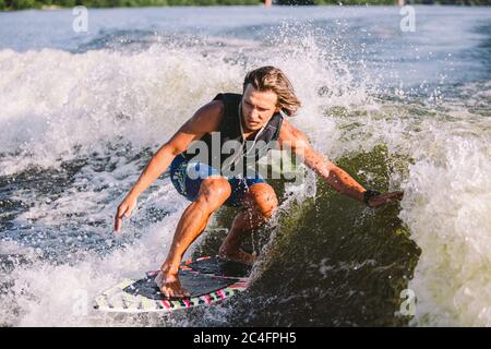 Belle wakesurf blonde aux cheveux longs en gilet à bord le long des vagues du lac. Un athlète sportif se réveille en surfant sur la rivière en été. Eau de Wakesurf Banque D'Images