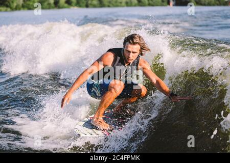 Belle wakesurf blonde aux cheveux longs en gilet à bord le long des vagues du lac. Un athlète sportif se réveille en surfant sur la rivière en été. Eau de Wakesurf Banque D'Images