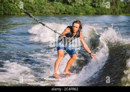 Belle wakesurf blonde aux cheveux longs en gilet à bord le long des vagues du lac. Un athlète sportif se réveille en surfant sur la rivière en été. Eau de Wakesurf Banque D'Images