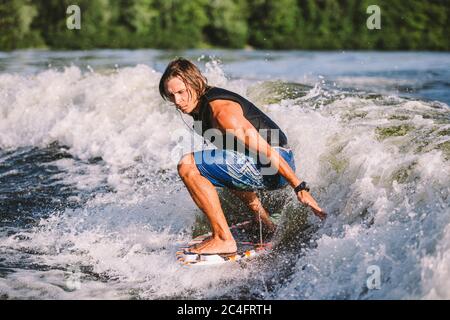 Belle wakesurf blonde aux cheveux longs en gilet à bord le long des vagues du lac. Un athlète sportif se réveille en surfant sur la rivière en été. Eau de Wakesurf Banque D'Images