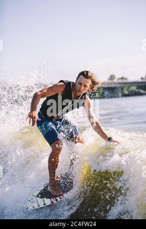 Belle wakesurf blonde aux cheveux longs en gilet à bord le long des vagues du lac. Un athlète sportif se réveille en surfant sur la rivière en été. Eau de Wakesurf Banque D'Images