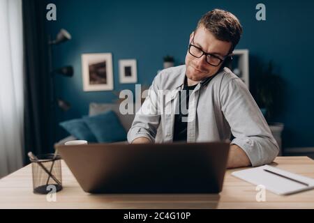Homme souriant travaillant sur un ordinateur portable et parlant sur un smartphone Banque D'Images