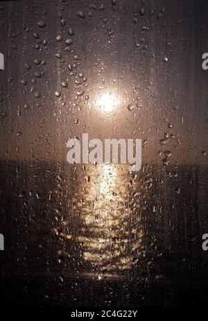 Gouttes d'eau sur la fenêtre de verre contre le beau coucher de soleil dans la mer Banque D'Images