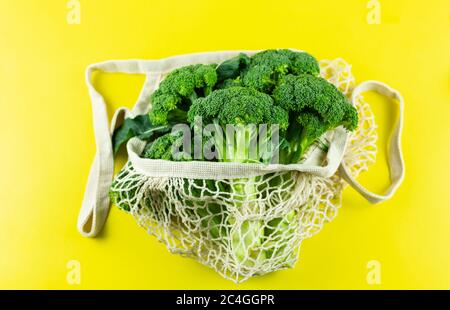 Brocoli frais dans un sac blanc écologique sur fond jaune. Hass avocat dans un sac de filet de déchets zéro. Concept sans plastique. Copier l'espace Banque D'Images