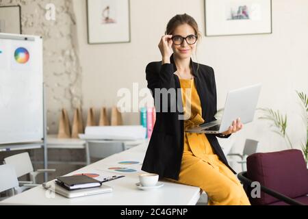 Jeune femme belle en lunettes et veste noire assise sur Banque D'Images