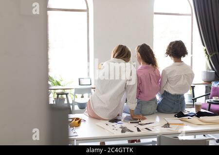 Groupe de jeunes femmes élégantes de derrière assis sur le bureau pendant que dre Banque D'Images
