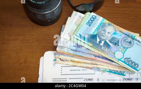 Objectif de la caméra, argent étranger et carte d'embarquement sur une table en bois. Tourisme, vacances, équipement de photographie de voyage. Banque D'Images