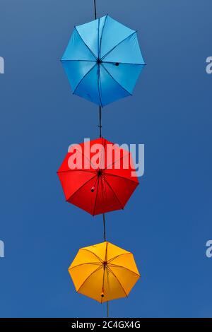 Vue à angle bas de trois parasols de couleur différente, rouge, orange et bleu, suspendus sur un câble contre un ciel bleu clair. Banque D'Images