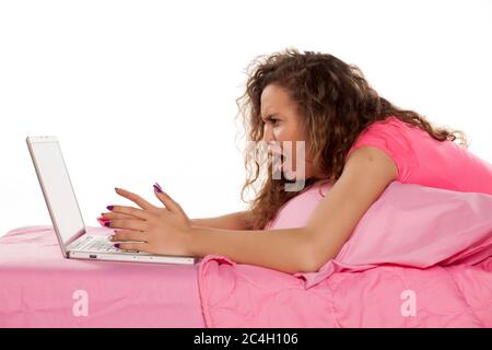 jeune femme nerveuse et en colère, couchée au lit avec un ordinateur portable sur fond blanc Banque D'Images