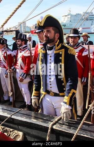 Malaga, Espagne - 26 octobre 2014 : capitaine de la Marine royale du XVIIIe siècle à bord d'un navire avec son équipage. Les gens derrière avec l'uniforme de marine royale, co rouge Banque D'Images