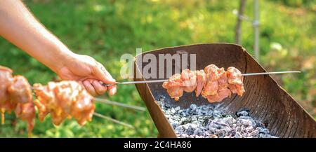 Mains de l'homme prépare la viande de barbecue sur brochette au gril au feu à l'extérieur Banque D'Images