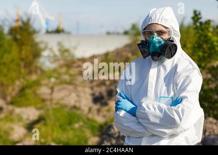 Portrait de la jeune femme en vêtements de travail et masque de protection debout avec les bras croisés et regardant la caméra elle travaille dans une zone dangereuse Banque D'Images