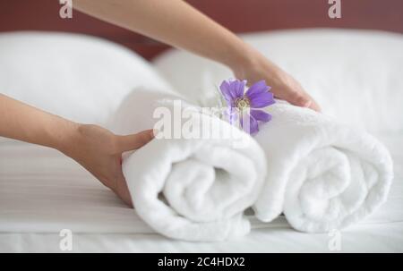 Femme de ménage plaçant un ensemble de serviettes blanches et une fleur sur un lit d'hôtel. Banque D'Images