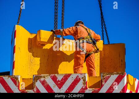 Un ingénieur portant une combinaison orange et un casque rigide guide le contrepoids de grue mobile en position Banque D'Images