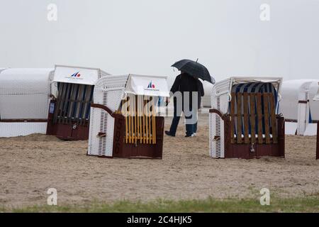 Harlesiel/Carolinensiel, Allemagne juin 2020: Images symboliques - 2020 vacanciers marchent avec leurs parasols à travers les paniers de plage sur la plage de Carolinensiel-Harlesiel sous la pluie. Météo | utilisation dans le monde entier Banque D'Images