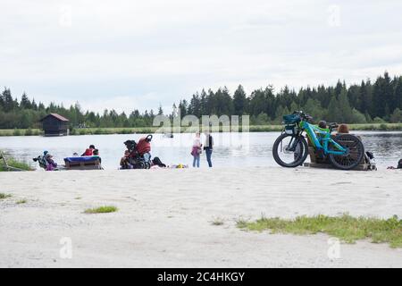 Fichtelberg, Allemagne. 21 juin 2020. Fichtelgebirge, Allemagne 06/21/2020: Images symboliques - 2020 deux vélos e-bike/pedelec sont sur un banc, en arrière-plan deux personnes sont assis sur un banc et regardent le Fichtelsee. D'autres personnes courent le long du lac. | utilisation dans le monde crédit : dpa/Alay Live News Banque D'Images