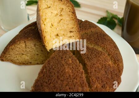 Tranché, divisé tarte éponge en portionsand une tasse de café avec du lait sur un fond en bois. Une pièce est prise et posée sur le dessus. Minimaliste. Banque D'Images
