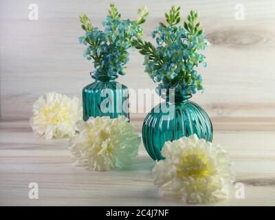 Deux vases en verre vert sarcelle remplis de fleurs d'hortensia sarcelle avec fleurs de carnation blanches alignées devant elles sur un fond en bois. Si Banque D'Images