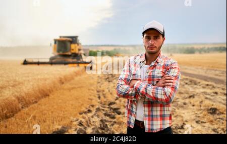 Heureux fermier fièrement debout dans un champ avec les bras croisés sur la poitrine. Le conducteur de la moissonneuse-batteuse va récolter du blé riche. Port agronome Banque D'Images