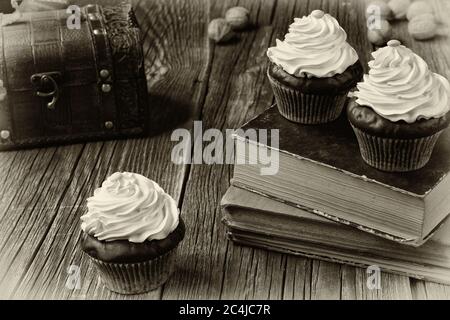 Les petits gâteaux dans les étuis à patty en papier sont couchés sur des vieux livres et des planches de bois abîmés. Une poitrine et quelques coques de noix... UN effet photo noir et blanc. Banque D'Images