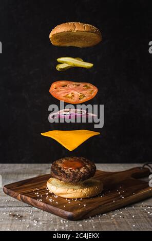 Hamburger avec ingrédients flottants séparés sur fond noir. Banque D'Images