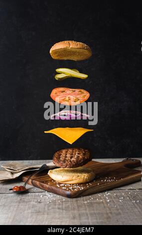 Hamburger avec ingrédients flottants séparés sur fond noir. Banque D'Images