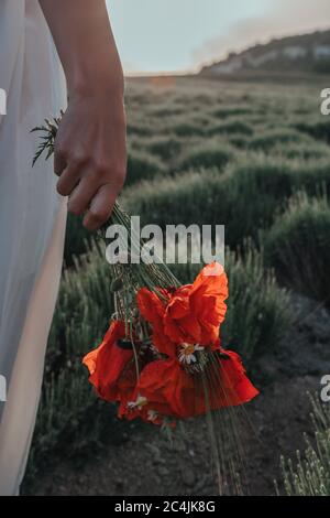 Mariée dans une robe blanche tenant un bouquet de fleurs de pavot, temps chaud de coucher de soleil sur le fond du champ de lavande. Copier l'espace. Le concept de Banque D'Images