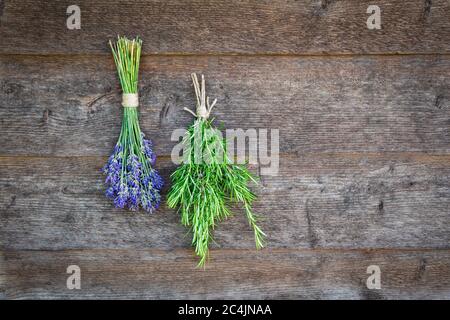 Des faisceaux de fleurs de lavande fraîches et d'herbes de romarin sèchent et pendent à l'envers sur un mur en bois. Banque D'Images