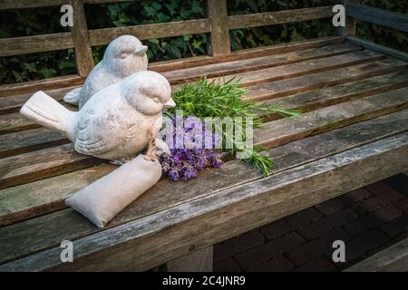 Banc de jardin décoré avec des oiseaux de pierre et des herbes aromatiques en été. Banque D'Images