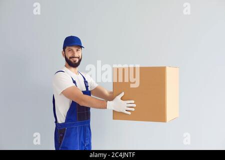 Joyeux jeune livreur tenant boîte carton avec maquette pour votre conception sur fond gris Banque D'Images