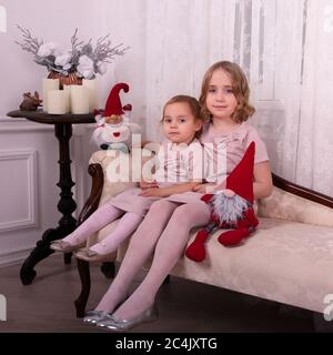 Deux petites sœurs attendent Noël. Les filles sont assises près des gnomes. Elles sont habillées de robes roses à paillettes Banque D'Images