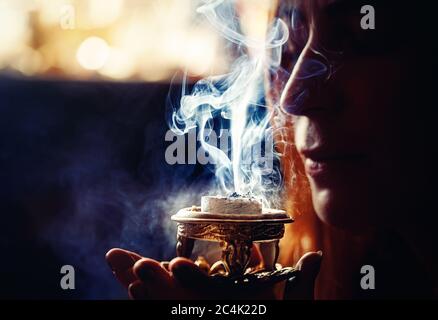 encens dans une main de femme, fumée d'encens sur fond noir. Banque D'Images