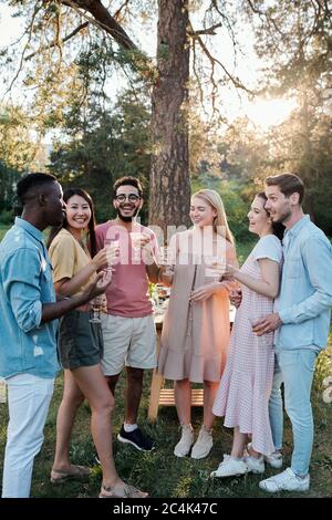 Jeunes hommes et femmes gais de diverses origines ethniques qui applaudissent avec des verres de vin et écoutent un gars africain qui se fait des toasts Banque D'Images