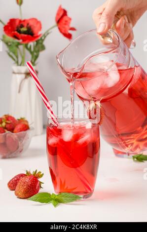 Une femme verse une boisson rafraîchissante d'été avec des fraises et de la glace à partir d'un détanter. Photo verticale Banque D'Images