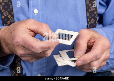 un homme âgé tient des mains de 35 mm de diapositives de vieilles photos dans ses mains rugueuses suggérant la mémoire Banque D'Images