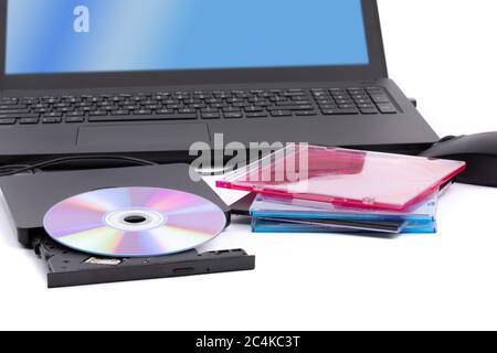 Un lecteur de CD DVD externe ouvert avec une pile de boîtiers de CD et un ordinateur portable en arrière-plan Banque D'Images