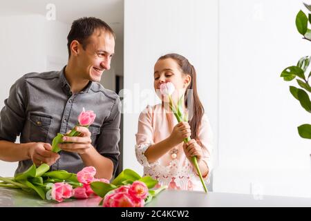 Le père tient sur ses mains petite fille sur fond clair à l'intérieur. Portrait de papa avec fleurs et fille. Le concept de vacances en famille. Père Banque D'Images