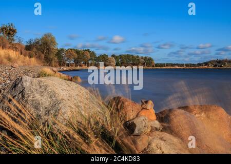 Plage sur l'île de Ruegen sur la mer Baltique. Horizon bleu sous le soleil d'automne. Pierres et herbes au premier plan. Arbres sur la côte Banque D'Images