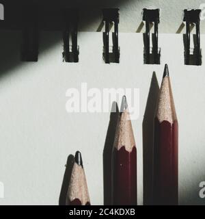 Trois pointes de crayon pointant vers une ceinture en spirale sur une surface blanche éclairée par la lumière naturelle Banque D'Images