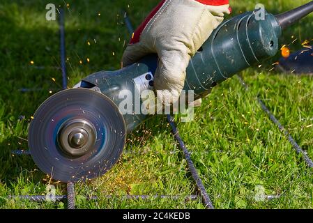 Coupe du filet métallique avec une meuleuse sur l'herbe verte. Étincelles provenant de matériaux de contact. À l'extérieur, couper le filet d'acier. Utiliser une meuleuse d'angle. Banque D'Images