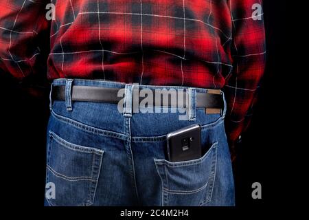 un homme en jean bleu et une chemise à carreaux rouges avec téléphone cellulaire dans la poche arrière sur fond noir Banque D'Images