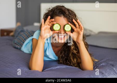 Belle femme fait le soin de beauté à la maison avec le concombre. Banque D'Images