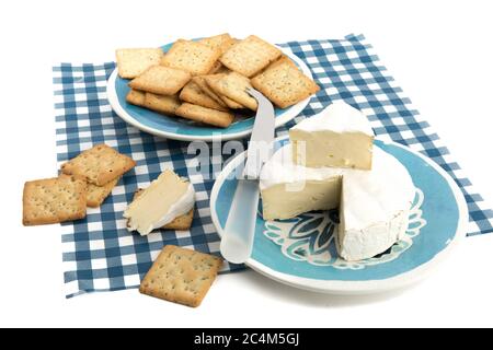 un rond de brie avec un morceau découpé avec des craquelins multigrains sur une nappe à carreaux bleus Banque D'Images