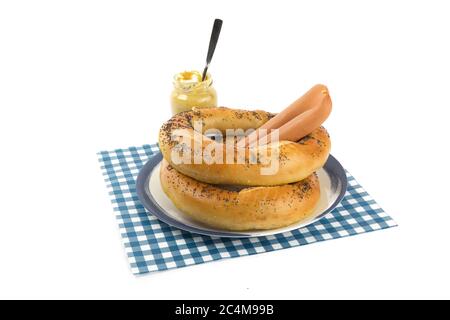 deux grands bagels bretzel et deux hot dogs sur une assiette bleue et un pot de moutarde isolé sur blanc Banque D'Images